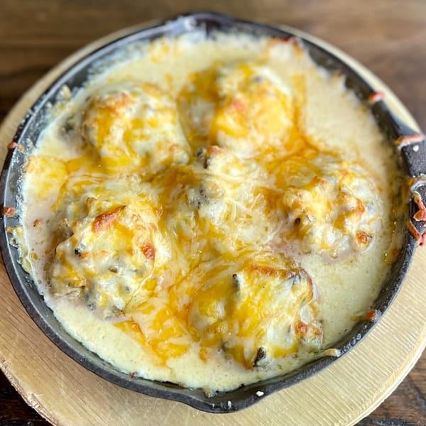 A cast iron skillet filled with cheesy, creamy baked meatballs, served on a wooden trivet.