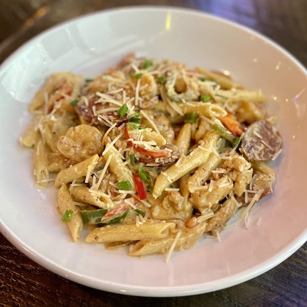 Creamy penne pasta with shrimp, sausage, peppers, and shredded cheese in a white bowl.