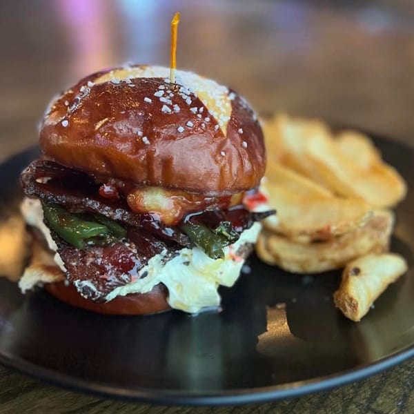 A SouthTown PourHouse burger with bacon, jalapenos, and cream cheese on a pretzel bun, with fries.