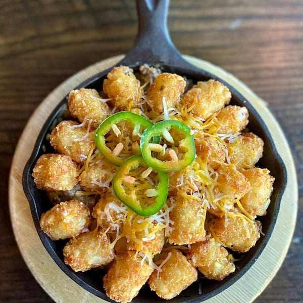 Crispy tater tots topped with shredded cheese and sliced jalapeños in a cast iron skillet.