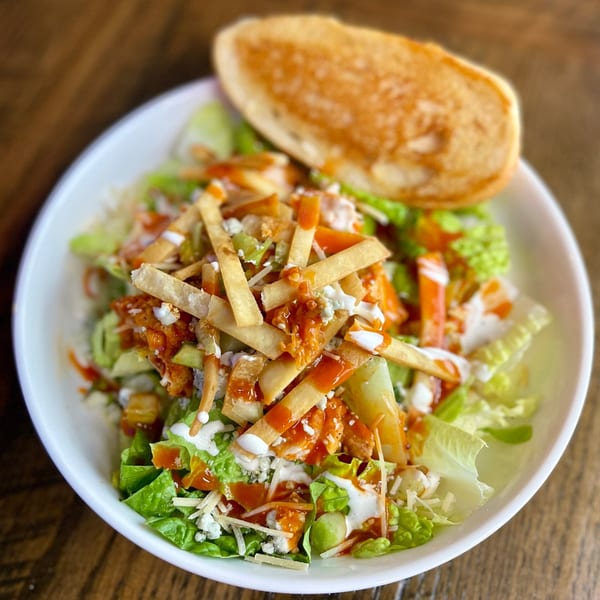 A buffalo chicken salad with tortilla strips, blue cheese, and ranch dressing, served with toast.